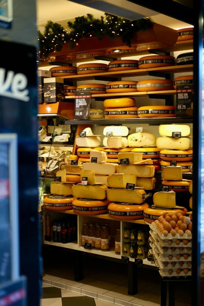 Shelves filled with different types of cheeses in a cheese shop, showcasing a variety of cheese wheels and blocks.