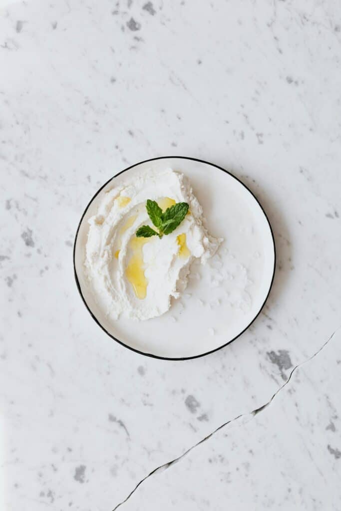 A serving of cottage cheese on a white plate, drizzled with olive oil and garnished with fresh mint, set on a marble countertop.