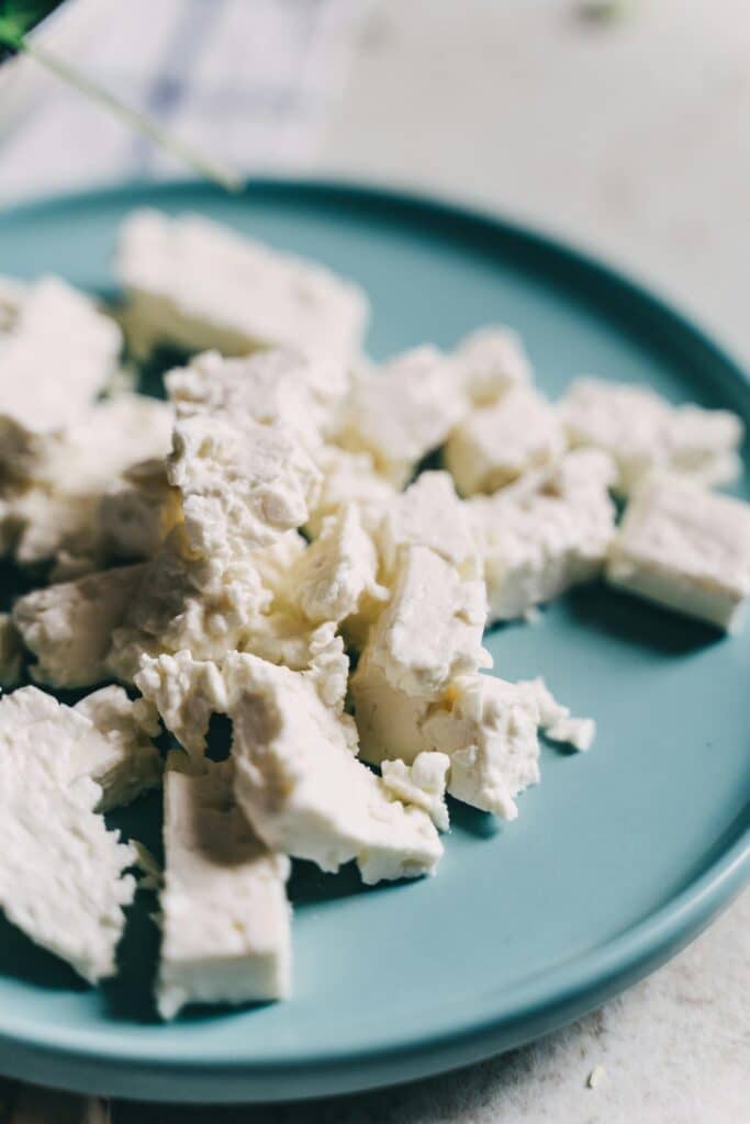 Crumbled pieces of feta cheese on a blue plate, showcasing its creamy texture.