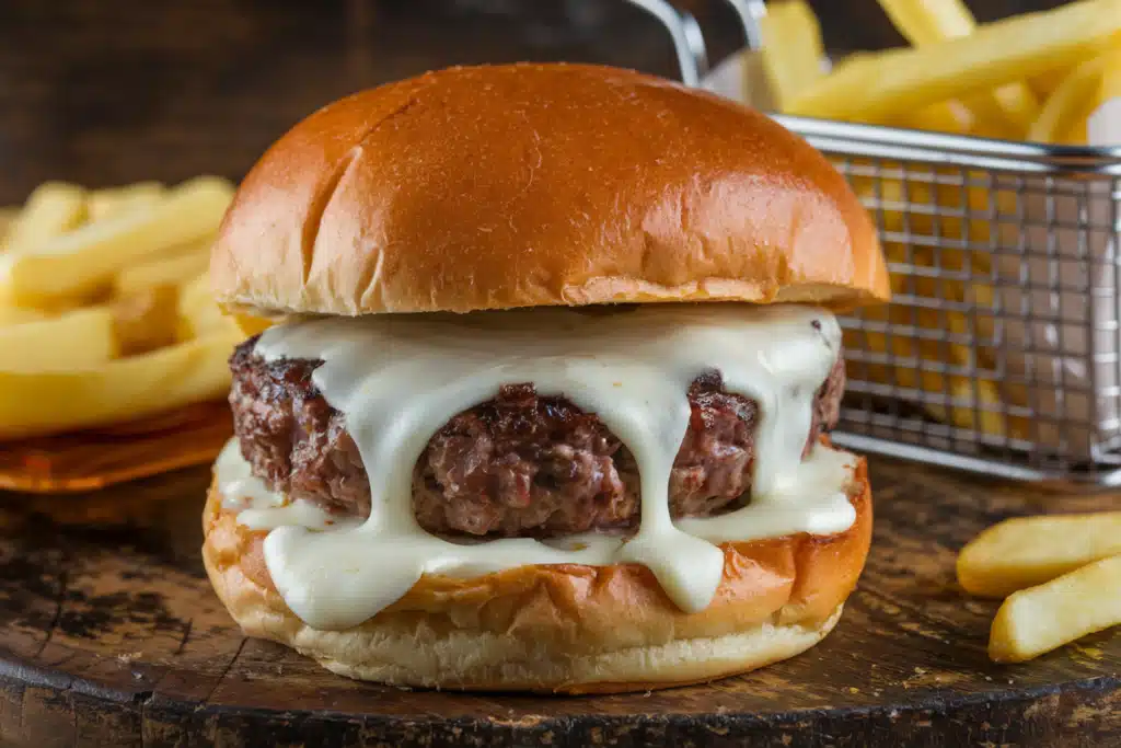 Cheeseburger with melted cheese dripping over the patty, served with a side of fries.