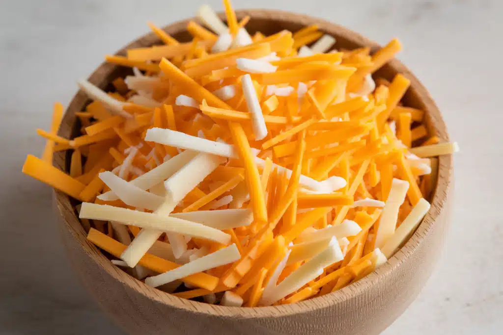 Wooden bowl filled with shredded yellow and white cheese.